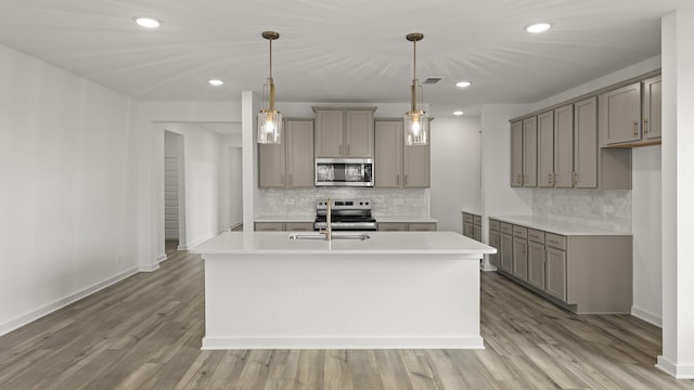 kitchen with pendant lighting, light hardwood / wood-style floors, stainless steel appliances, and an island with sink