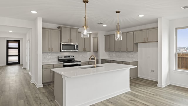 kitchen featuring stainless steel appliances, hanging light fixtures, sink, and a center island with sink