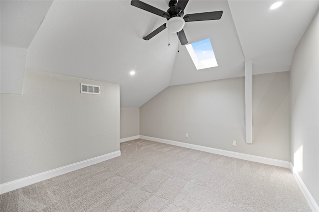 additional living space with ceiling fan, light colored carpet, and lofted ceiling with skylight