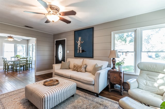 living room featuring dark hardwood / wood-style floors, plenty of natural light, wooden walls, and ceiling fan