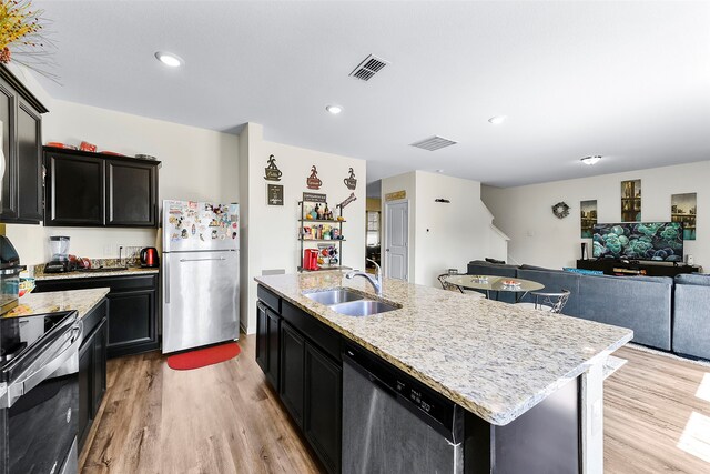 kitchen with light hardwood / wood-style floors, an island with sink, light stone countertops, stainless steel appliances, and sink