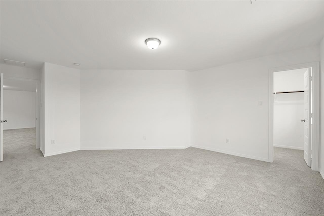 unfurnished bedroom featuring a walk in closet, a closet, and light colored carpet