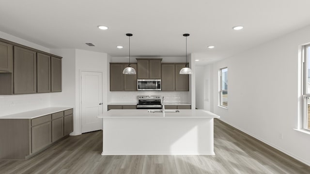 kitchen with sink, tasteful backsplash, decorative light fixtures, a center island with sink, and appliances with stainless steel finishes