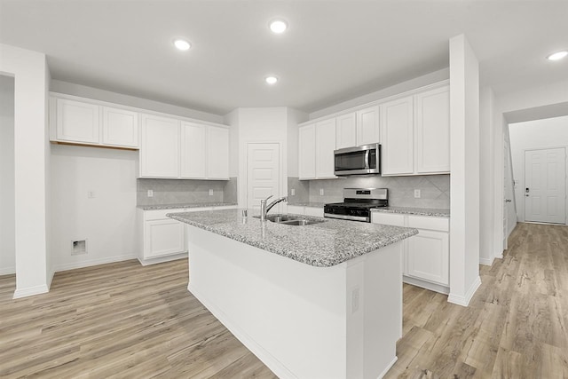 kitchen with light stone countertops, appliances with stainless steel finishes, sink, a center island with sink, and white cabinetry