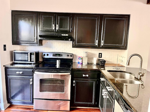 kitchen with under cabinet range hood, a sink, appliances with stainless steel finishes, tasteful backsplash, and dark stone countertops