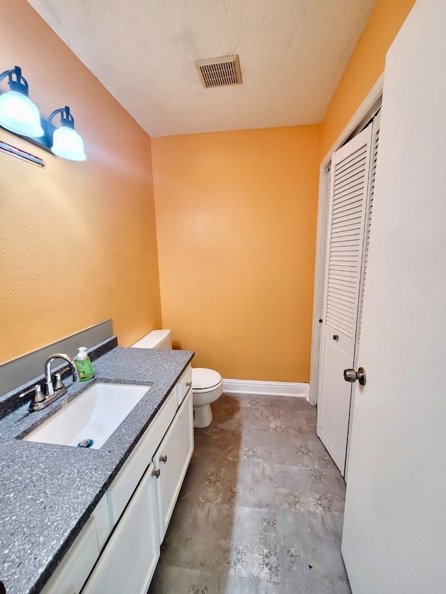 bathroom featuring a textured ceiling, vanity, toilet, and concrete flooring