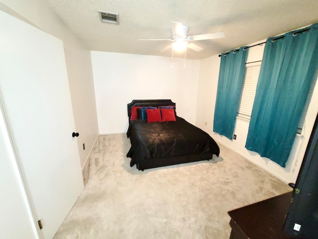 bedroom with ceiling fan, light colored carpet, and a textured ceiling