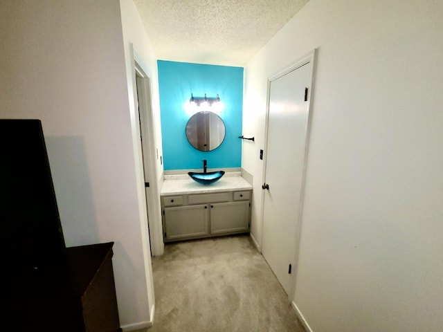 hallway with a textured ceiling, baseboards, a sink, and light colored carpet