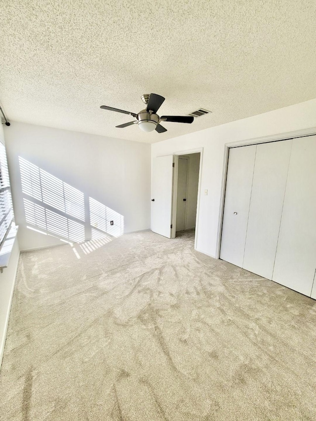 unfurnished bedroom featuring carpet, a closet, visible vents, a ceiling fan, and a textured ceiling