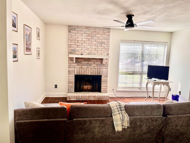 living room with ceiling fan, hardwood / wood-style flooring, a fireplace, and a textured ceiling