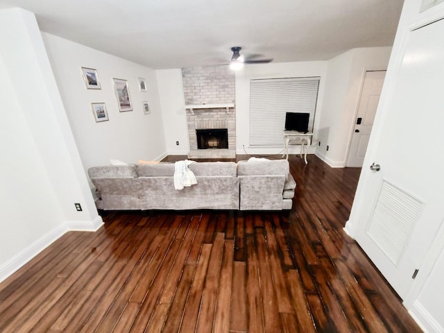 living room with dark wood-style flooring, a fireplace, a ceiling fan, and baseboards