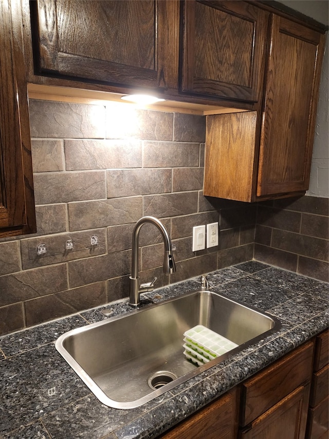 interior space featuring dark brown cabinets, backsplash, dark stone counters, and sink