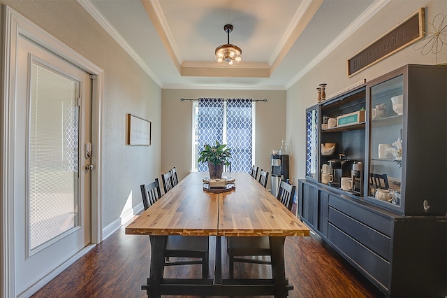 dining space with a raised ceiling, ornamental molding, and dark hardwood / wood-style flooring