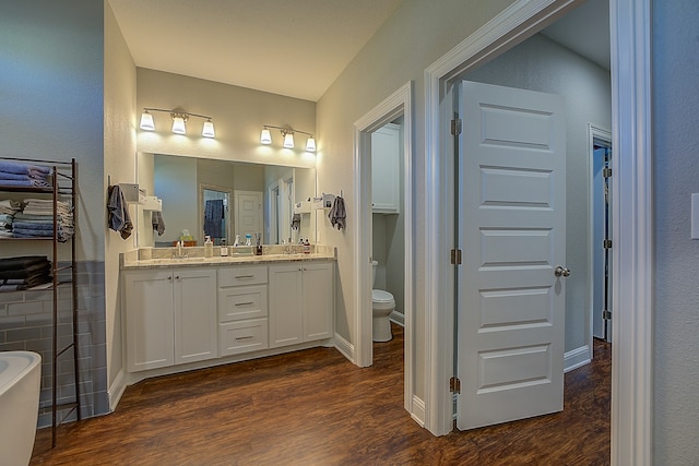 bathroom featuring a washtub, hardwood / wood-style flooring, vanity, and toilet