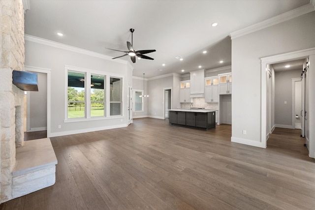 unfurnished living room with a stone fireplace, ceiling fan, ornamental molding, and dark hardwood / wood-style flooring