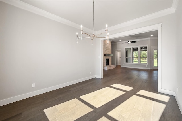 unfurnished dining area featuring ceiling fan with notable chandelier, dark hardwood / wood-style floors, ornamental molding, and a stone fireplace