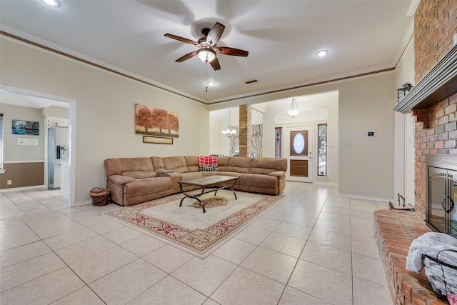 tiled living room with ceiling fan with notable chandelier, ornamental molding, and a brick fireplace