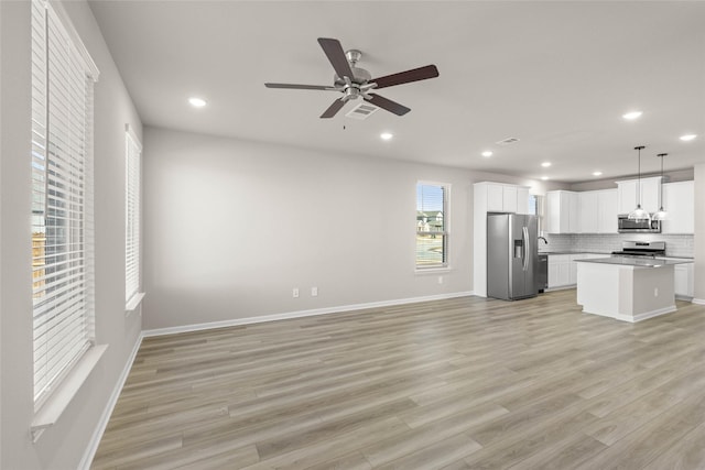 kitchen featuring appliances with stainless steel finishes, decorative light fixtures, tasteful backsplash, white cabinetry, and a center island