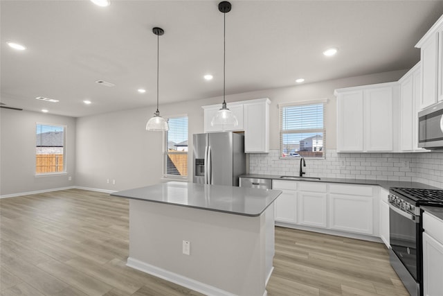 kitchen with pendant lighting, sink, appliances with stainless steel finishes, white cabinets, and a kitchen island