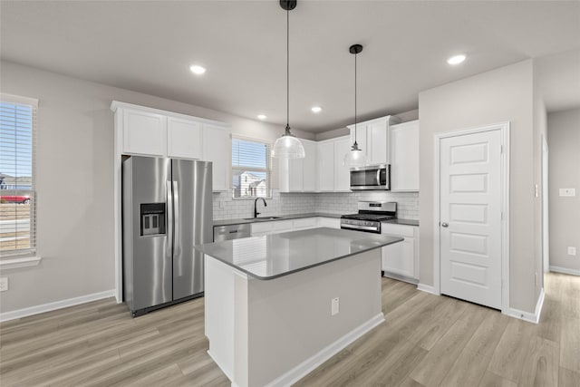 kitchen featuring a kitchen island, appliances with stainless steel finishes, decorative light fixtures, sink, and white cabinets