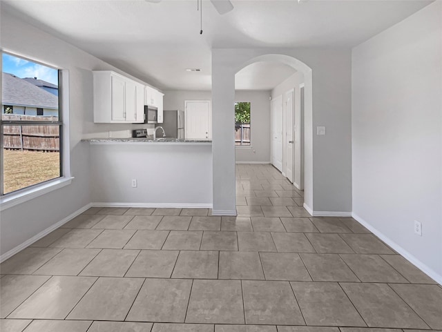 interior space with light stone counters, white cabinetry, kitchen peninsula, appliances with stainless steel finishes, and ceiling fan