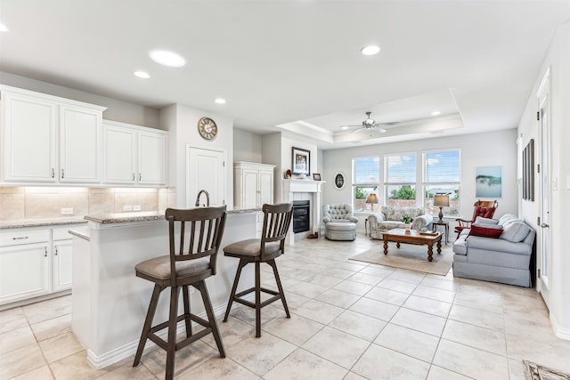 kitchen featuring white cabinets, ceiling fan, a tile fireplace, and a center island with sink