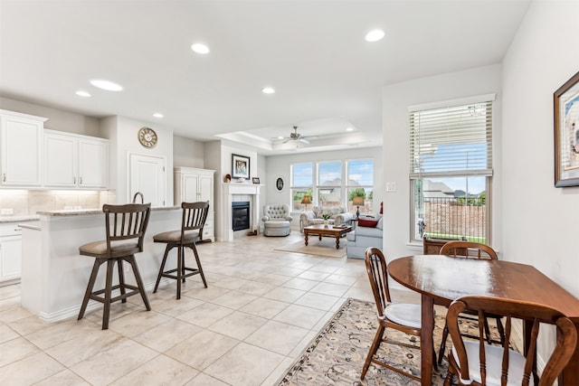 tiled dining area with a raised ceiling and ceiling fan