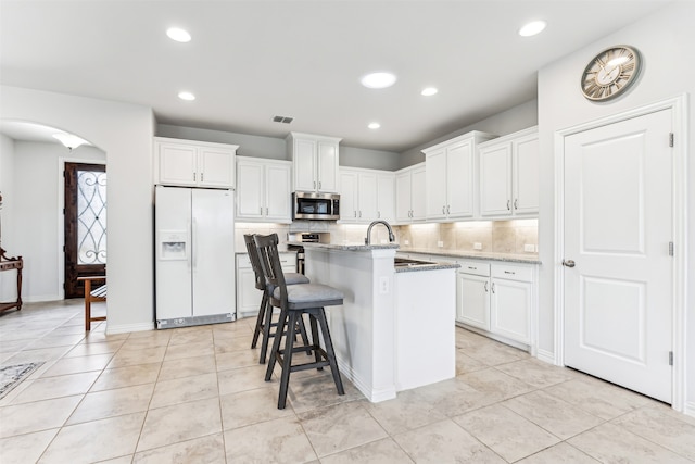 kitchen with appliances with stainless steel finishes, white cabinetry, a breakfast bar, light stone countertops, and a kitchen island with sink