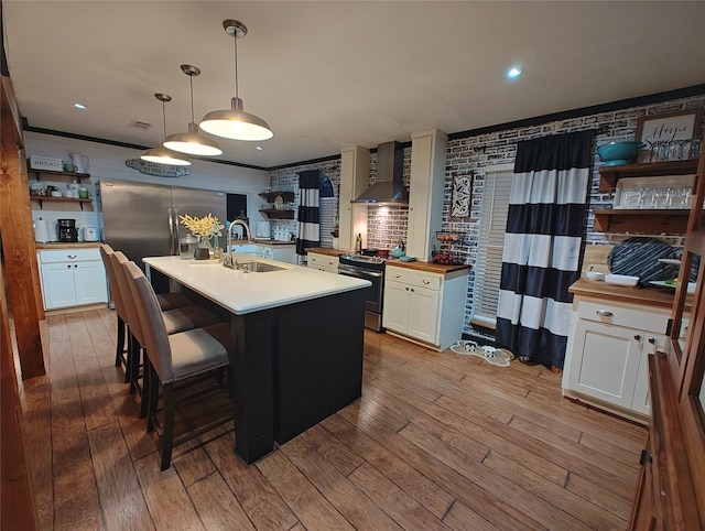 kitchen with a kitchen island with sink, sink, white cabinets, wall chimney range hood, and decorative light fixtures