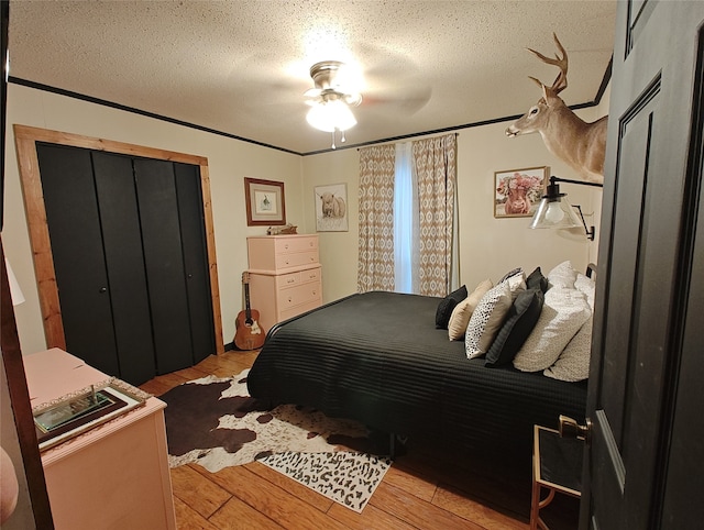 bedroom featuring ceiling fan, a textured ceiling, light hardwood / wood-style flooring, a closet, and crown molding