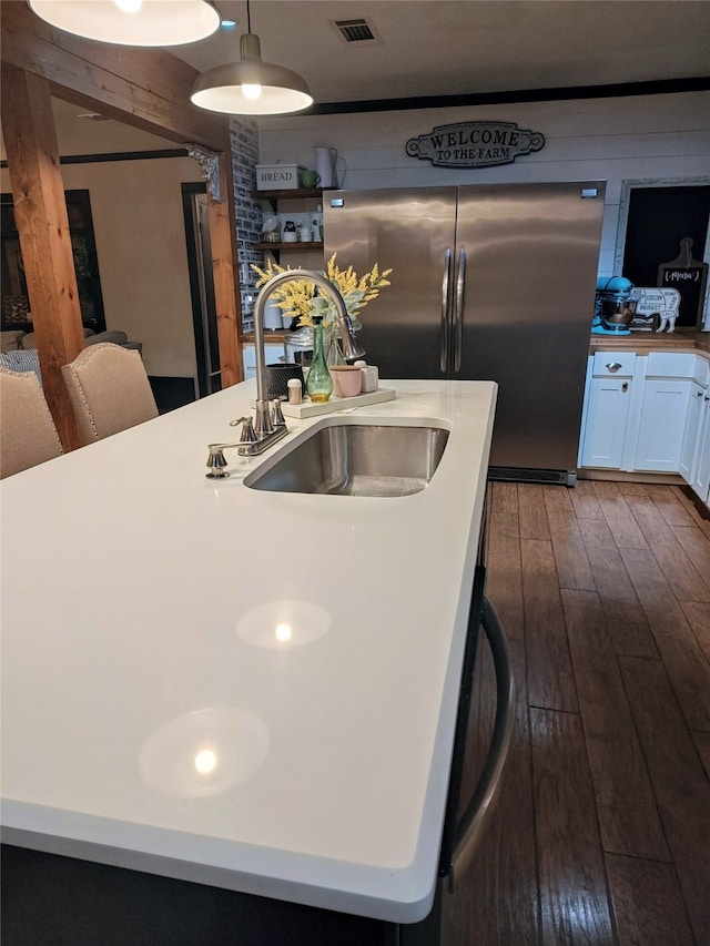 kitchen featuring stainless steel fridge, white cabinets, dark hardwood / wood-style flooring, decorative light fixtures, and sink