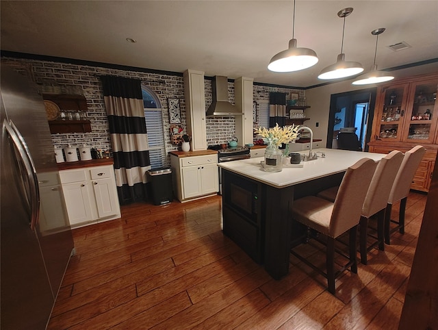 kitchen with pendant lighting, a center island with sink, wall chimney range hood, white cabinetry, and dark hardwood / wood-style floors