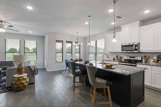 kitchen with pendant lighting, an island with sink, sink, stainless steel appliances, and ceiling fan with notable chandelier