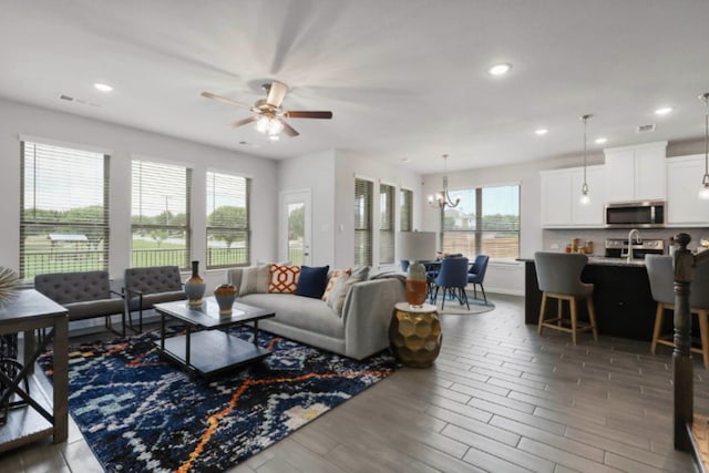 living room featuring a healthy amount of sunlight, ceiling fan with notable chandelier, and dark hardwood / wood-style flooring