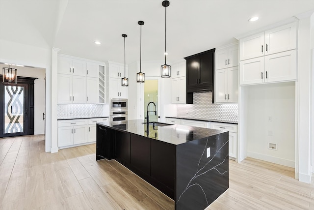 kitchen featuring sink, a kitchen island with sink, stainless steel appliances, light hardwood / wood-style floors, and decorative backsplash