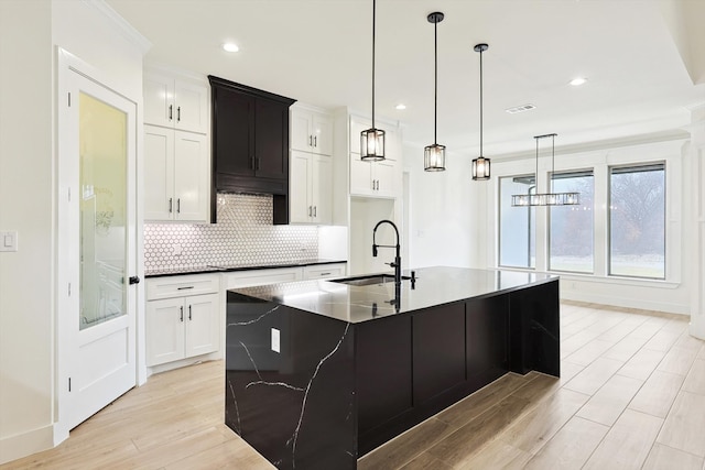 kitchen with white cabinets, light wood-type flooring, a kitchen island with sink, and sink