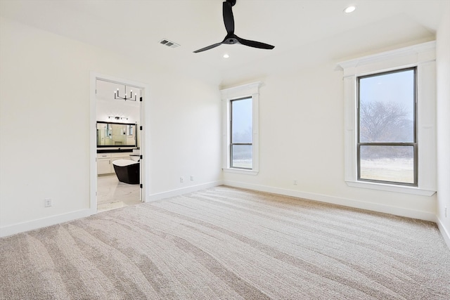 interior space featuring ceiling fan, ensuite bath, light carpet, and multiple windows