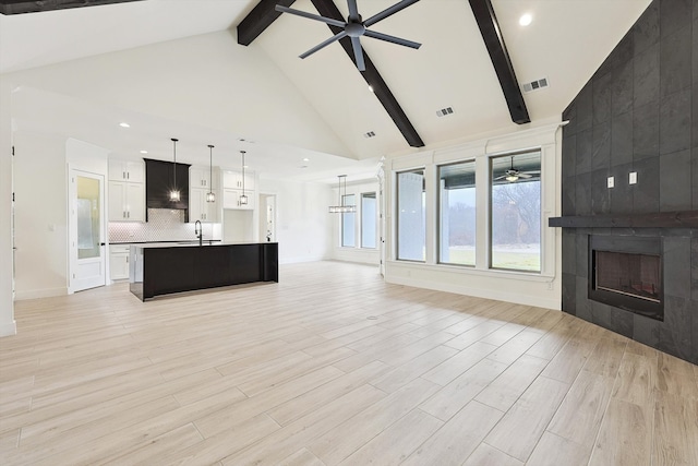 unfurnished living room featuring ceiling fan, beam ceiling, high vaulted ceiling, a tile fireplace, and light hardwood / wood-style floors