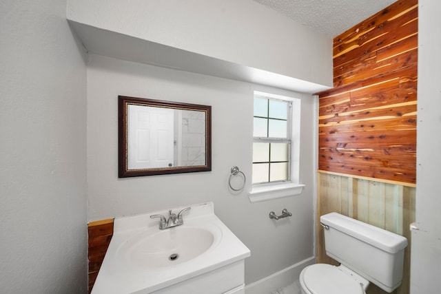 bathroom featuring wooden walls, a textured ceiling, vanity, and toilet