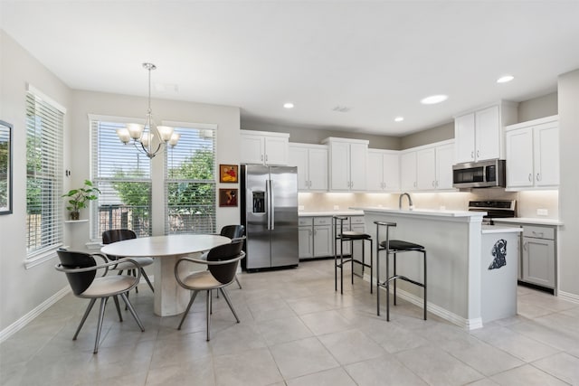 kitchen featuring appliances with stainless steel finishes, white cabinetry, pendant lighting, an inviting chandelier, and a kitchen island with sink