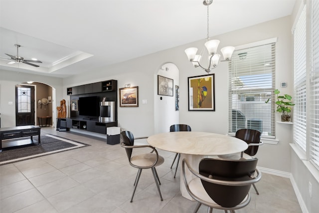 dining space featuring ceiling fan with notable chandelier, a fireplace, a tray ceiling, and plenty of natural light