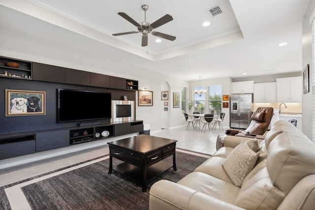 living room featuring sink, a tray ceiling, ceiling fan with notable chandelier, crown molding, and tile patterned flooring