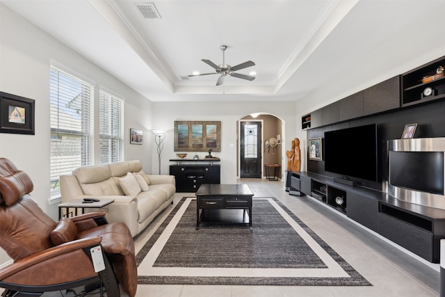 tiled living room with ornamental molding, a tray ceiling, and ceiling fan