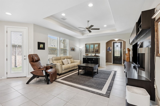 tiled living room with ornamental molding, ceiling fan, and a raised ceiling