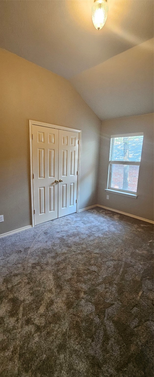 carpeted empty room with vaulted ceiling