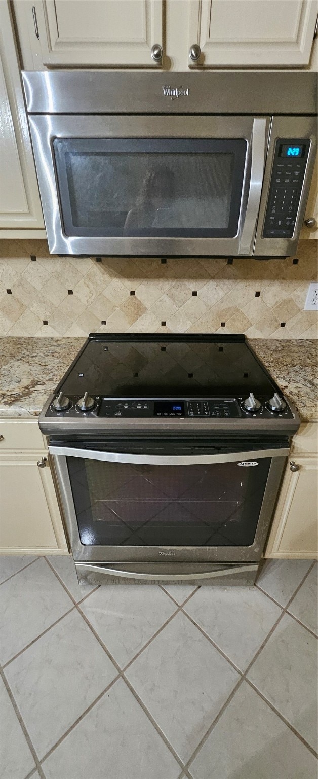 kitchen with light stone counters, cream cabinets, appliances with stainless steel finishes, and backsplash