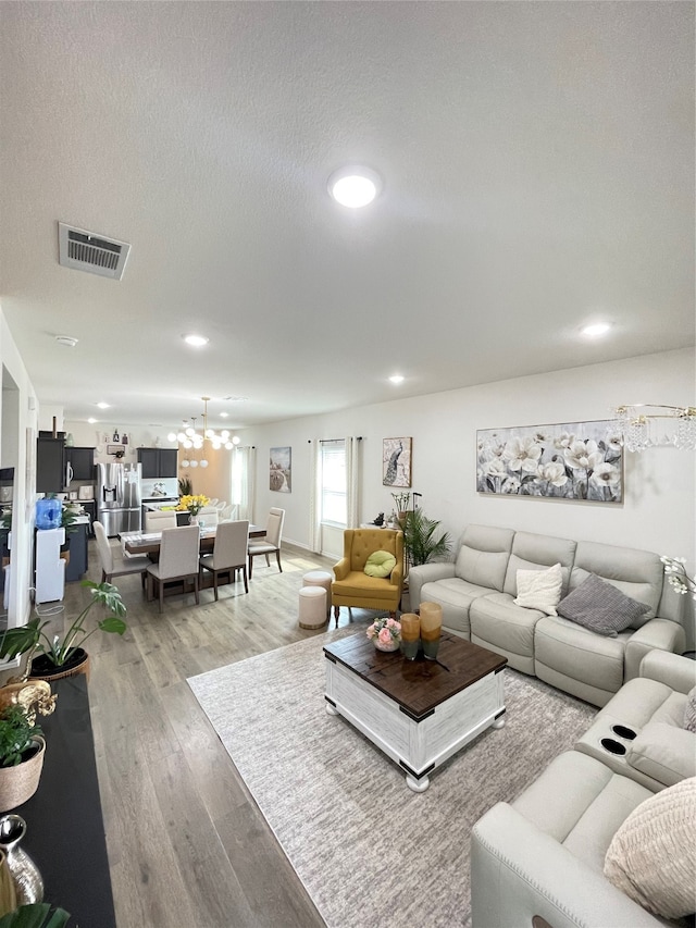 living room featuring light wood-type flooring, a notable chandelier, and a textured ceiling