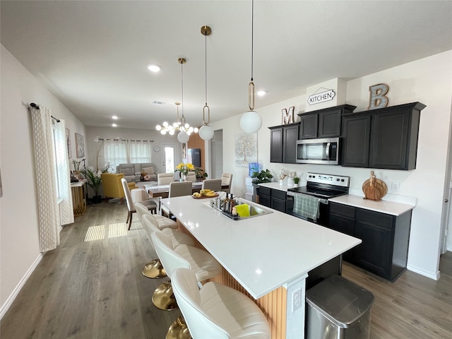 kitchen with light hardwood / wood-style floors, a kitchen island with sink, stainless steel appliances, and a kitchen bar