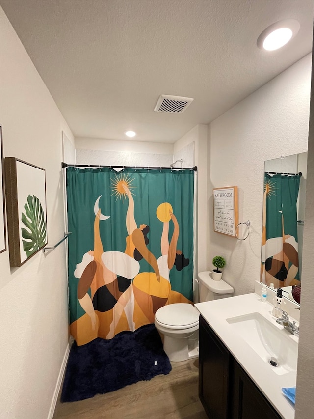 bathroom with vanity, a textured ceiling, hardwood / wood-style flooring, walk in shower, and toilet