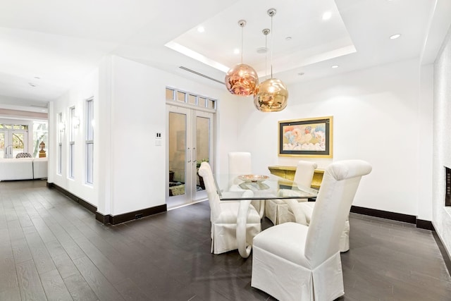 dining space with a tray ceiling, dark wood-type flooring, and french doors